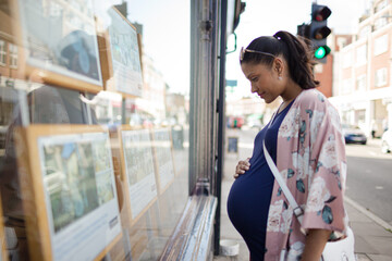 Pregnant woman browsing real estate listings at urban storefront