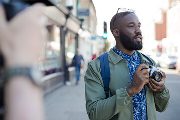 Smiling young male tourist with camera on urban street