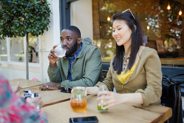 Smiling young friends drinking juice at sidewalk cafe