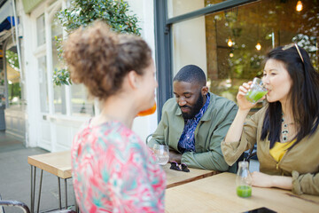 Smiling young friends drinking juice at sidewalk cafe