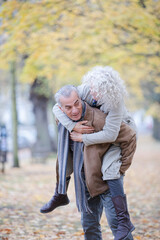 Senior man carrying woman on his back in autumn park