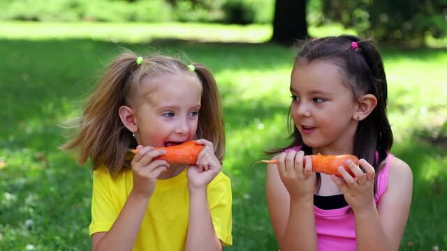 Two girls nibble raw carrots
