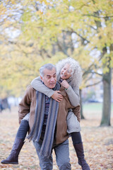 Fototapeta premium Senior man carrying woman on his back in autumn park