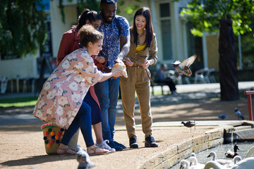 Fototapeta premium Friends feeding ducks and geese at sunny park pond