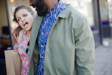 Affectionate young couple with shopping bag walking along storefront