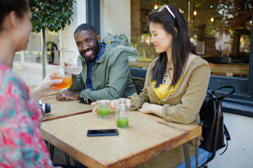 Smiling young friends drinking juice at sidewalk cafe
