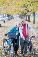 Senior couple walking bicycles among trees and leaves in autumn park