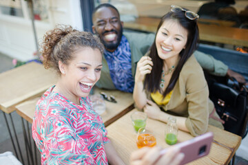 Smiling young friends taking selfie with camera phone at sidewalk cafe