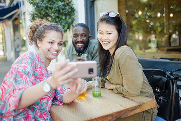 Smiling young friends taking selfie with camera phone at sidewalk cafe