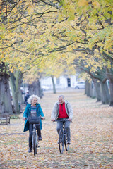 Senior couple bike riding among trees and leaves in autumn park