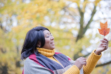 Senior woman holding orange autumn leaf in park