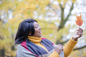 Senior woman holding orange autumn leaf in park