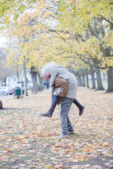 Fototapeta premium Senior man carrying woman on his back in autumn park