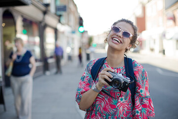 Portrait laughing, enthusiastic young female tourist in sunglasses photographing with camera on urban street