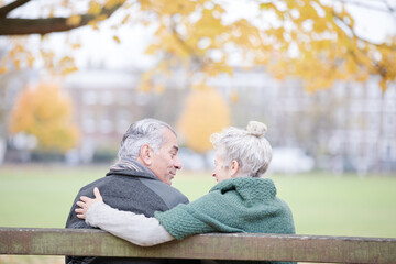 Carefree, affectionate senior couple hugging on bench in autumn park