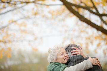 Smiling, affectionate senior couple hugging on bench in autumn park