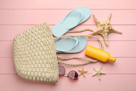 Stylish bag and beach accessories on pink wooden background, flat lay
