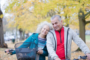 Senior couple walking bicycles among trees and leaves in autumn park