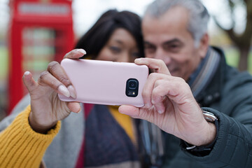 Smiling senior couple taking selfie in autumn park in front of red telephone booths