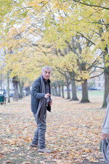 Obraz premium Senior man smiling amoung leaves in autumn park