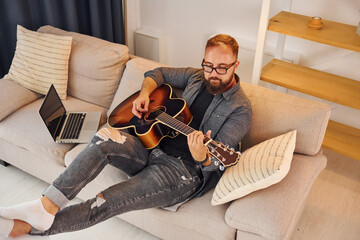 Having good time practicing. Man in casual clothes and with acoustic guitar is indoors