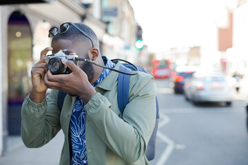 Young male tourist photographing with camera on urban street