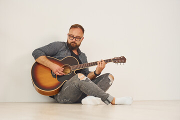 Obraz premium In the studio. Man in casual clothes and with acoustic guitar is indoors