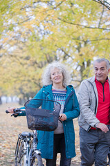 Obraz na płótnie Canvas Senior couple walking bicycles among trees and leaves in autumn park