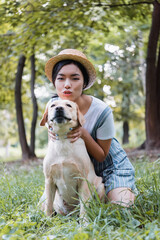 asian woman looking at camera while hugging labrador dog in park
