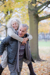 Fototapeta premium Senior man carrying woman on his back in autumn park