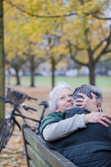 Smiling, affectionate senior couple hugging on bench in autumn park