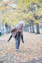 Fototapeta premium Senior man carrying woman on his back in autumn park