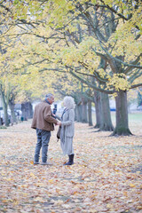 Fototapeta na wymiar Affectionate senior couple holding hands, walking among trees and leaves in autumn park