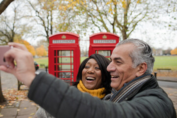 Smiling senior couple taking selfie in autumn park in front of red telephone booths
