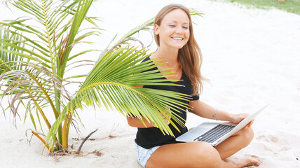 Blond girl with a laptop on tropical beach, freelance concept.