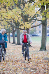 Senior couple bike riding among trees and leaves in autumn park