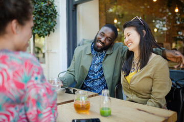 Woman photographing affectionate couple friends with camera phone at sidewalk cafe