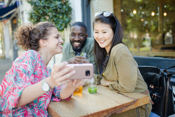 Smiling young friends taking selfie with camera phone at sidewalk cafe