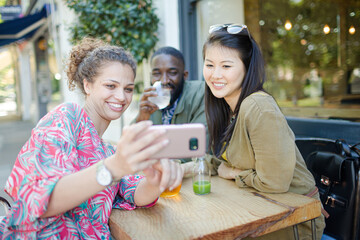 Smiling young friends taking selfie with camera phone at sidewalk cafe