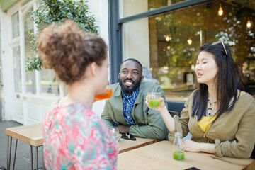 Smiling young friends drinking juice at sidewalk cafe