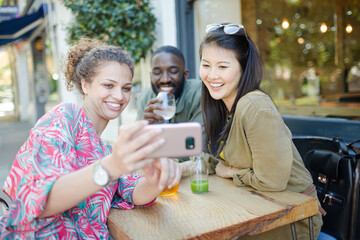 Smiling young friends taking selfie with camera phone at sidewalk cafe