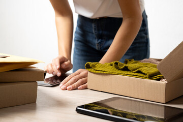 Woman packaging garment orders,cheking information on the smartphone.Small business.Fashion e-commerce