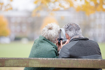 Happy senior couple sharing headphones, listening to music in park