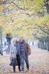 Fototapeta premium Affectionate couple hugging, walking among trees and leaves in autumn park