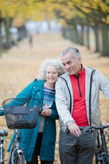 Senior couple walking bicycles among trees and leaves in autumn park