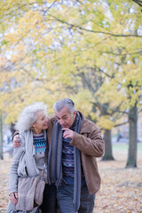 Affectionate couple hugging, walking among trees and leaves in autumn park