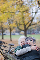 Smiling, affectionate senior couple hugging on bench in autumn park