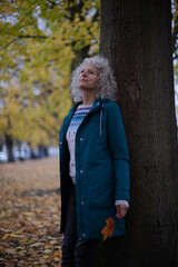 Serene senior woman leaning against tree in autumn park