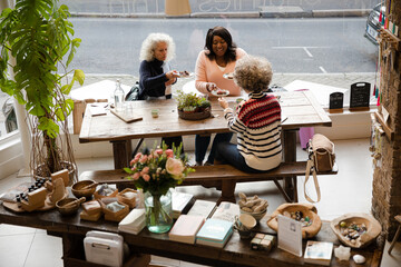 Laughing active senior women friends sharing dessert at autumn park cafe