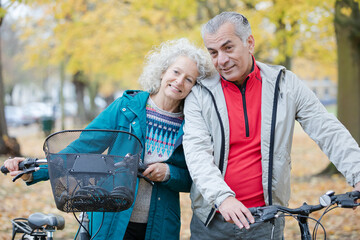 Senior couple walking bicycles among trees and leaves in autumn park